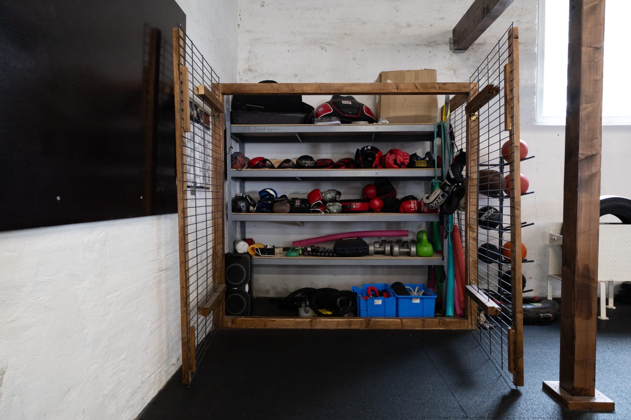 Regal mit Leih-Ausrüstung: Kopfschutz, Boxhandschuhe und Kurzhanteln, geordnet auf Fächern