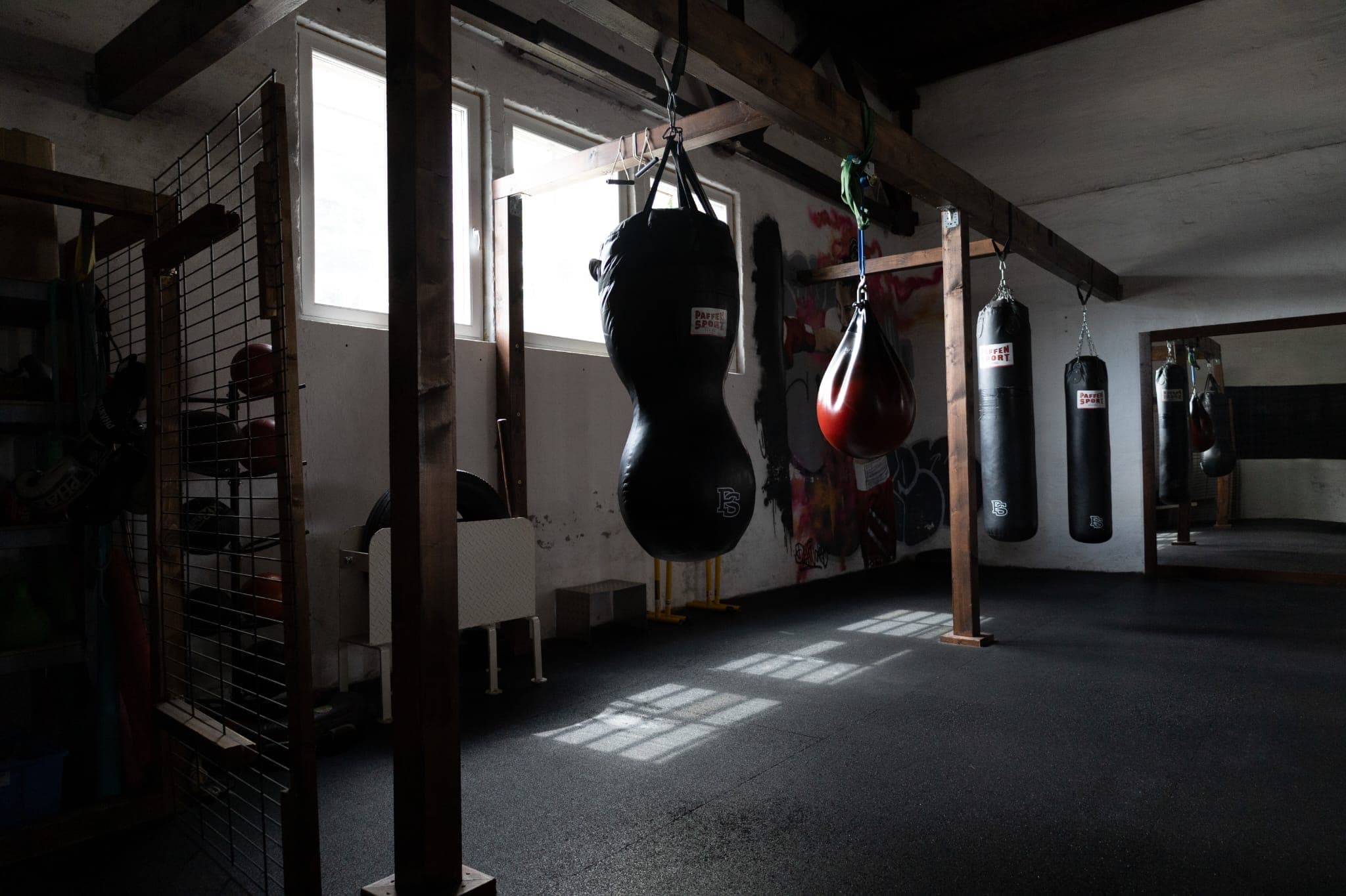 Boxsackraum mit Sandsack, Speedball und weiteren Sandsäcken vor hohen Fenstern